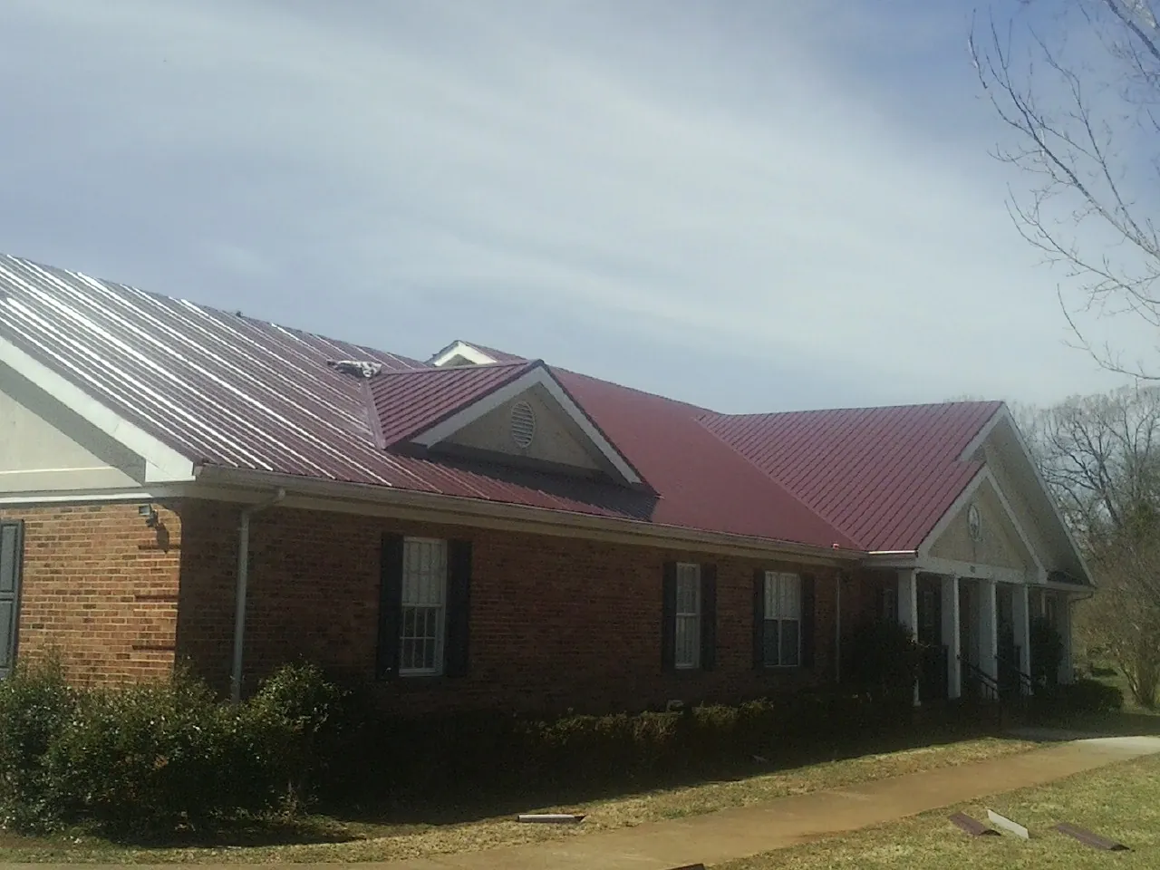 Red metal roof with gabled entries on a long brick building, from a Hail Damage Roof Repair job in Arcanum