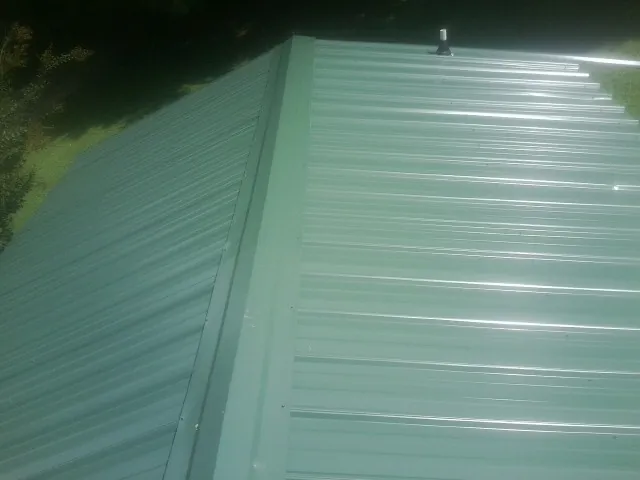 New green metal panels meeting at the ridge of a roof — Flat Roof Repair work by our crew in Arcanum