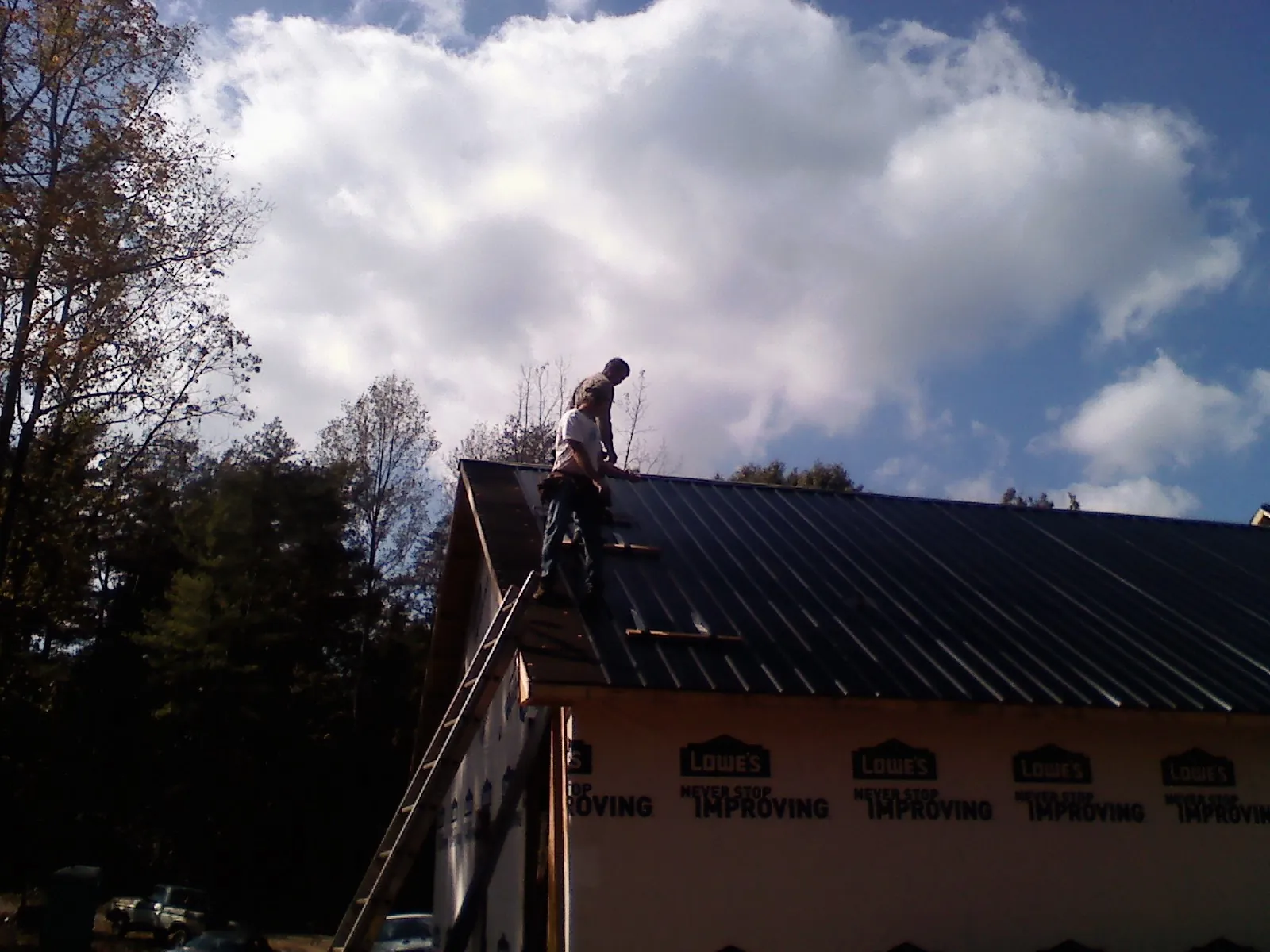 Roofer fastening dark metal panels high against a cloudy sky, from a Roof Inspection job in Arcanum