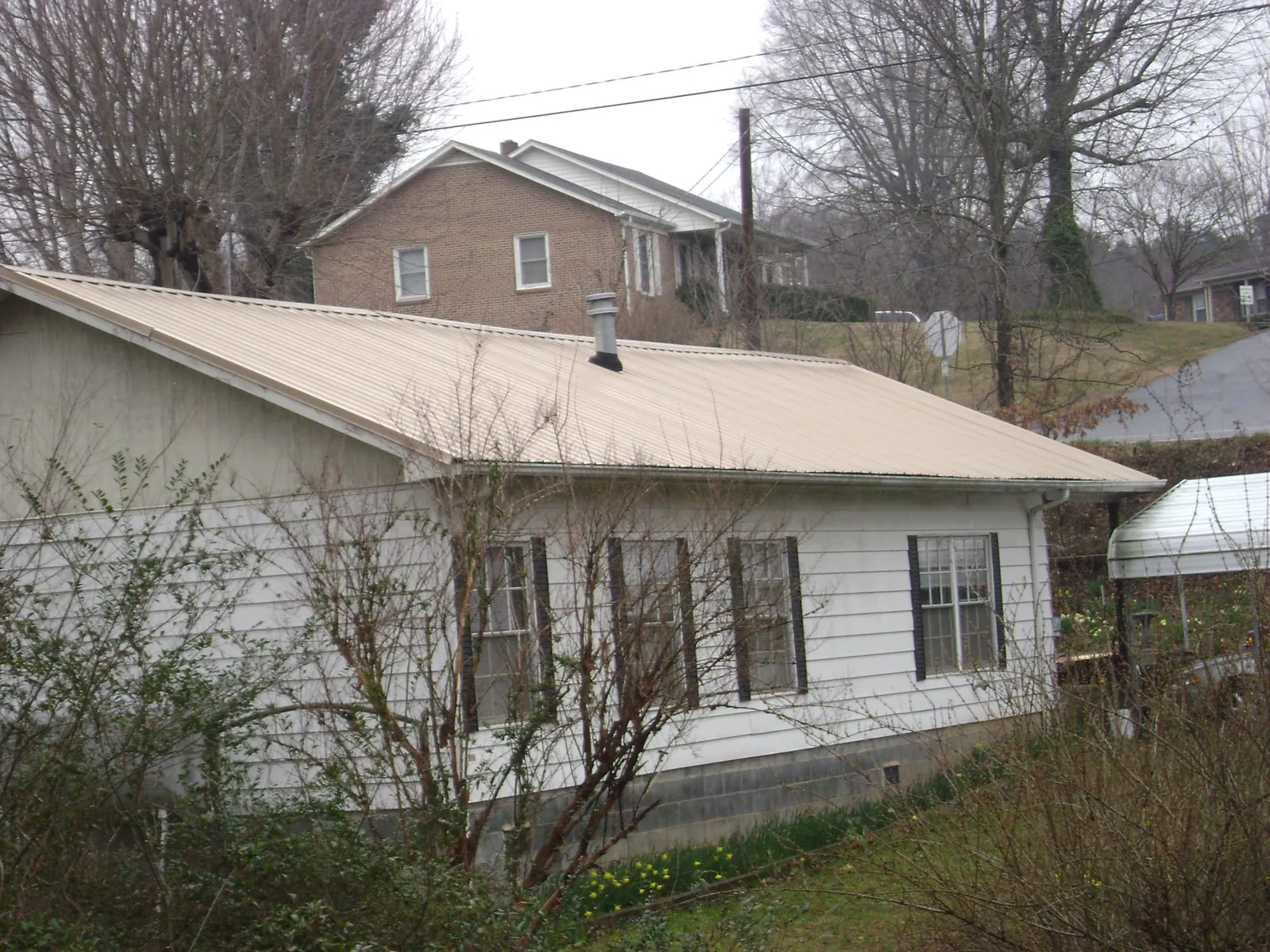 Tan metal roof on a white sided house set into a hillside — Commercial Roofing by Roofing Brothers in Arcanum