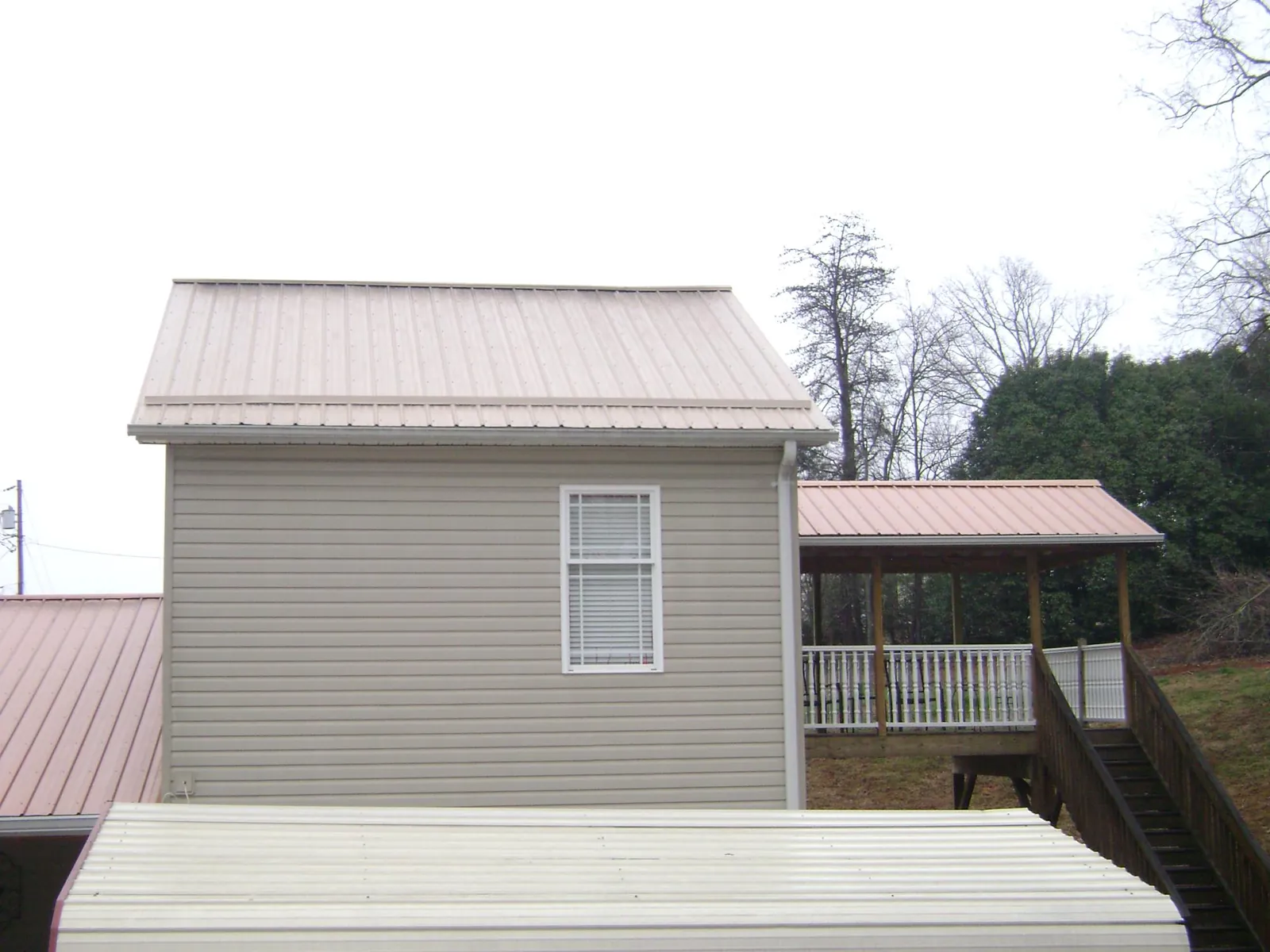 Tan metal roofs on a two story addition and attached porch, from a Roof Replacement job in Arcanum